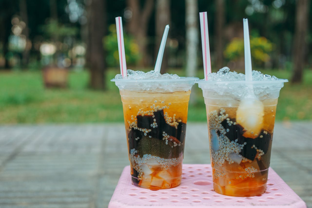services-02 Two iced beverages with toppings in plastic cups sitting outdoors on a pink table.