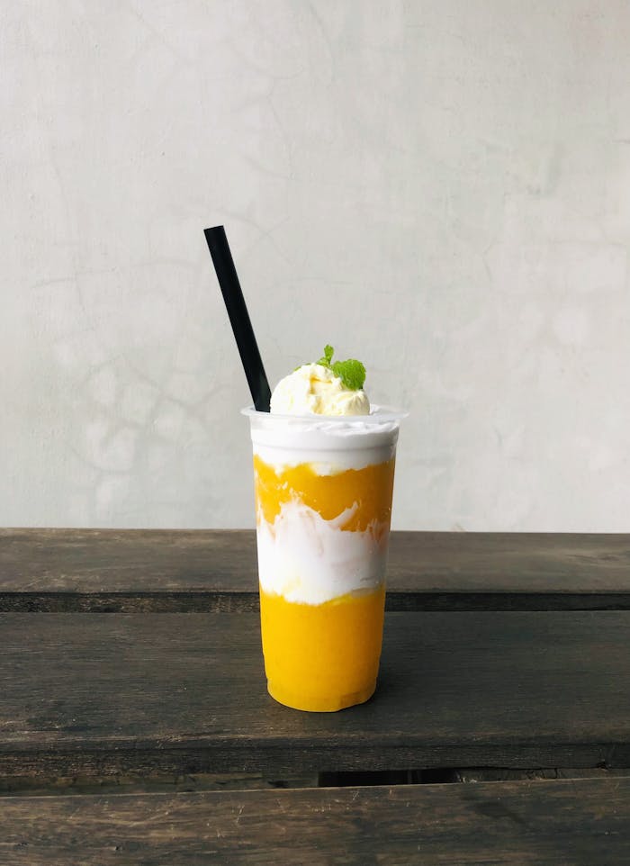 gallery-2 A vibrant mango juice with cream and a straw, perfect for a refreshing beverage.