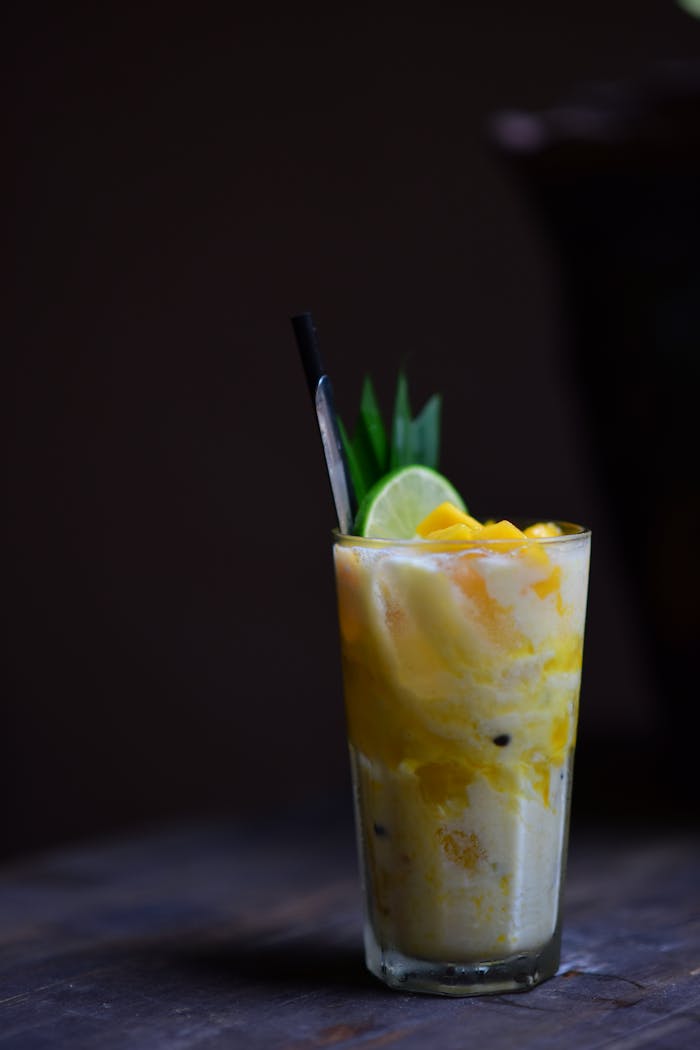 gallery-5 Delicious mango pineapple smoothie with lime garnish on a wooden table.