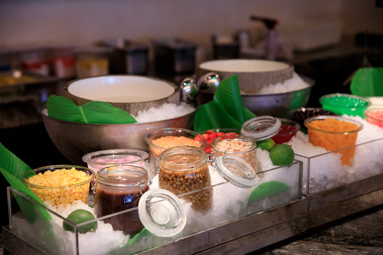 services-01 Assorted dessert toppings in jars on ice, ready for serving at a buffet counter.