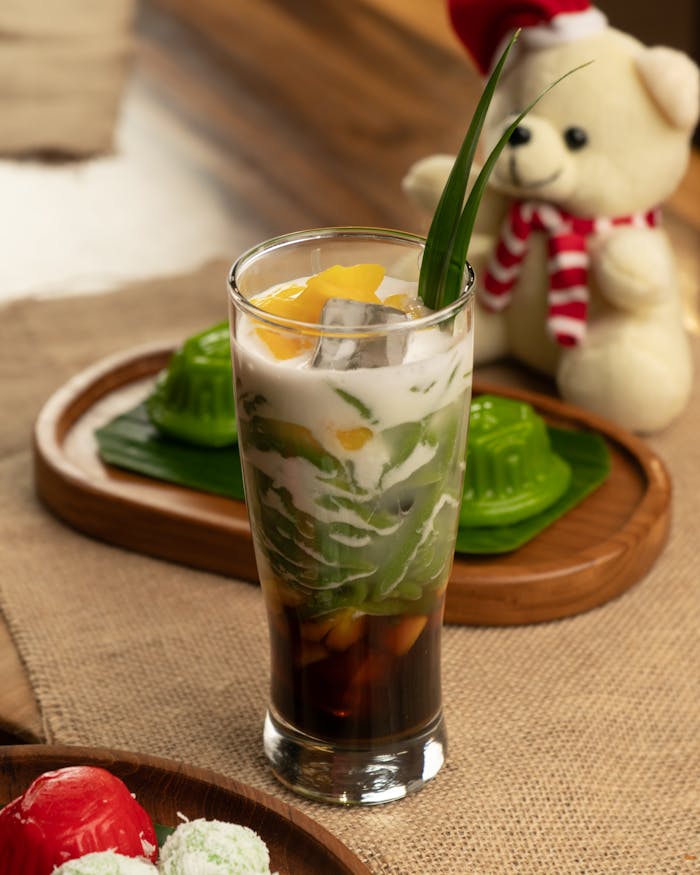 services-03 A colorful glass of Vietnamese Chè topped with pandan leaf and surrounded by festive decor.