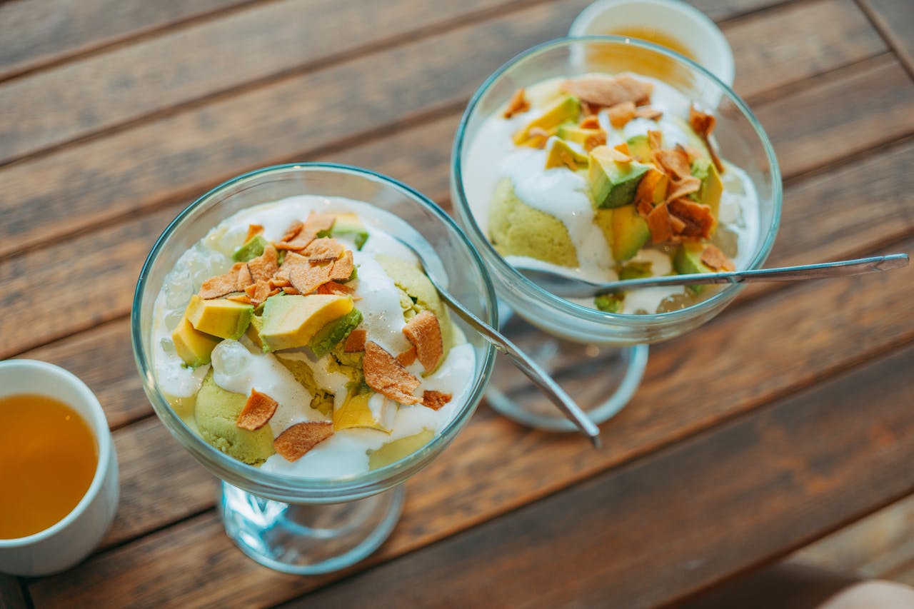 gallery-1 Top view of avocado dessert with cream in glass bowls on wooden table.